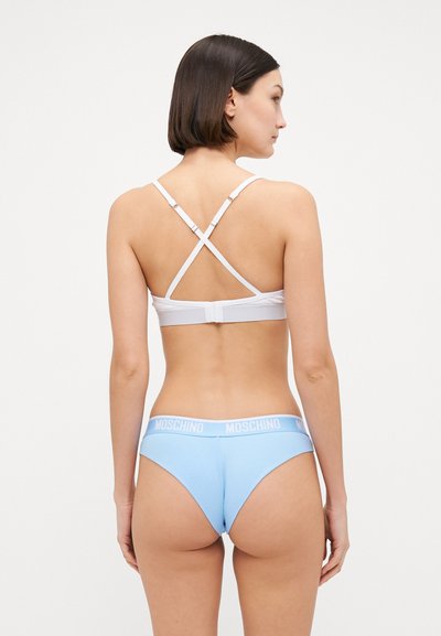 Biely podprsenka s prekríženými ramienkami, modré bikiny so spodkom s bielym pásom Moschino, bezšvový dizajn, hladké textúry a priliehavý strih.