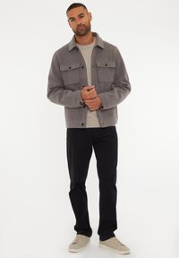 Grå uldblandingsjakke med to brystlommer og krave, parret med en lys sweater og sorte bukser. Cremefarvede sneakers fuldender outfittet.