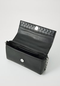 Svart läderclutch med quiltat lock, silverdetaljer och knappstängning. Inuti finns flera fack för organisering.