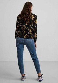 Floral long-sleeve top with a black background, paired with light blue denim jeans. Model wears patterned sneakers. Textured fabric details visible.