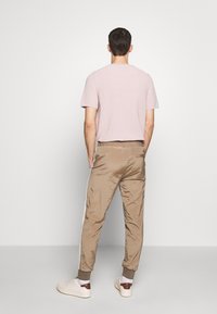 Camiseta de punto de manga corta en rosa claro combinada con pantalones jogger de seda color beige con rayas blancas laterales, cintura elástica y puños en los tobillos. Zapatillas blancas.