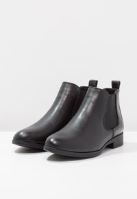 Bottines en cuir noir avec des panneaux latéraux élastiques, un bout rond et un petit talon empilé, avec une texture lisse et un design minimaliste.