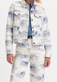 Modrá a bílá džínová bunda s malebným vzorem krajiny a zvířat. Krátký střih s předními kapsami a zapínáním na knoflíky.