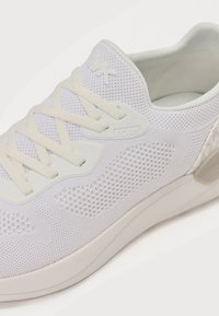 Weißer Sport sneaker mit Obermaterial aus Mesh, Schnürverschluss, strukturierten Seitenpaneelen und dezenter Markenkennzeichnung. Die glatte Sohle bietet leichtgewichtige Unterstützung.