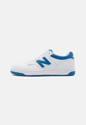 Baskets blanches basses avec des accents bleus, logo bleu "N" sur le côté, lacets blancs et bord de semelle bleu, présentées sur un fond uni.