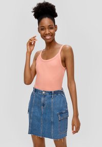 Débardeur rose clair à côtes associé à une mini-jupe en denim bleu avec une taille élastique, des poches latérales et un ourlet effiloché.
