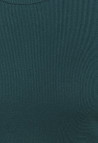 Ribbad linne i mörk teal, med rund halsringning och en elastisk textur, lämplig för layering eller avslappnad användning.