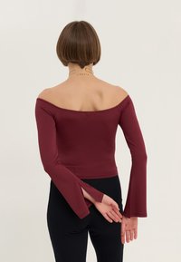 Burgundy off-shoulder topp med lång, utsvängd ärm. Slät, tight passform, med rektangulär skärning vid ärmsluten.