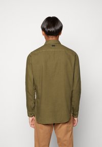 Oliivinvihreä pitkähihaisen paidan, jossa on kaulus, napilliset kalvosimet ja pyöristetty helma. Pinta on teksturoitu ja takana on merkki.