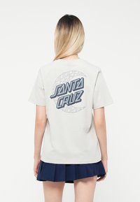 Tricou gri deschis cu grafică "SANTA CRUZ" pe spate, având un design circular și accente albastre. Material din bumbac, croi lejer.