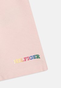 Jasnoróżowa bawełniana koszulka z krótkim rękawem, z haftem "HILFIGER" w wielokolorowych literach w prawym dolnym rogu. Miękka w dotyku.