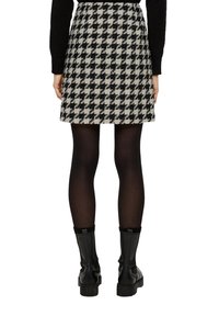 Wollen houndstooth miniskirt in zwart en wit. Heeft een uitlopende ontwerp. Gecombineerd met zwarte panty’s en zwarte knielaarzen.