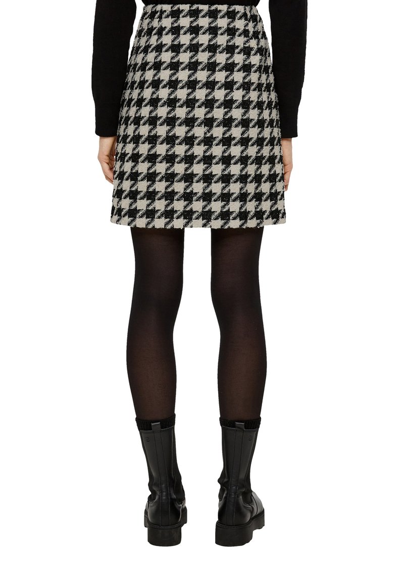 Mini spódnica w czarno-białą kratę houndstooth z wełny. Charakteryzuje się rozkloszowanym fasonem. Połączona z czarnymi rajstopami i czarnymi kozakami za kolano.