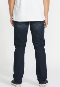 Jeans de mezclilla azul oscuro con corte recto, que presentan un diseño clásico de cinco bolsillos y una textura ligeramente desgastada.