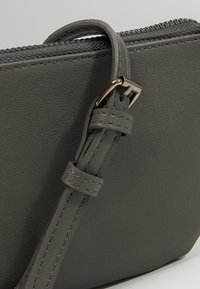 Borsa a tracolla in pelle grigia con una finitura testurizzata, forma rettangolare, tracolla regolabile e dettagli con zip in tonalità argentata.