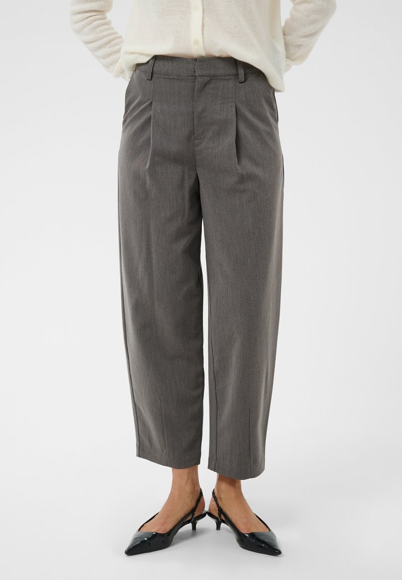 Pantalons gris sur mesure de longueur moyenne portés avec des talons slingback noirs pointus et un pull crème, montrés de la taille aux pieds.