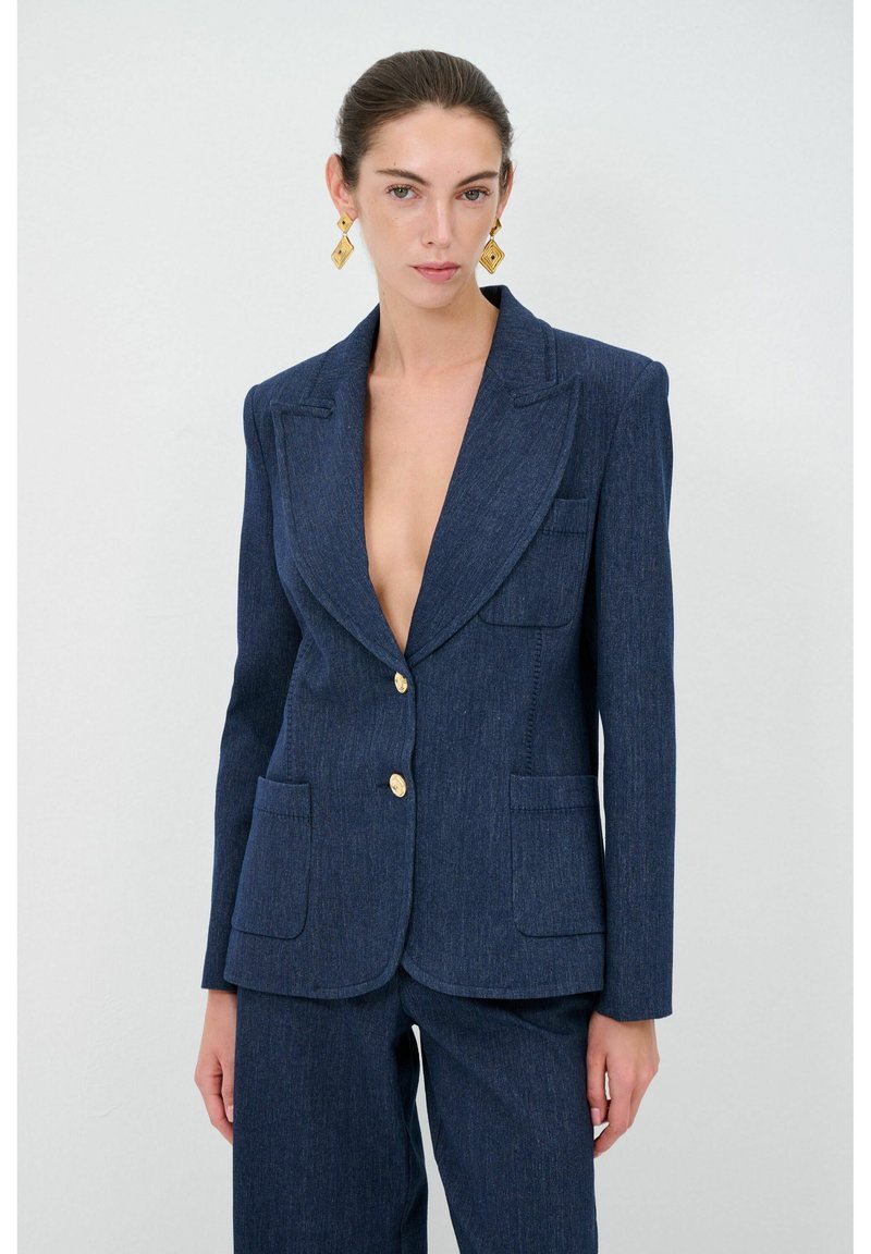Blazer aderente blu navy in tessuto testurizzato, con profondo scollo a V, due ampie tasche frontali e bottoni dorati.