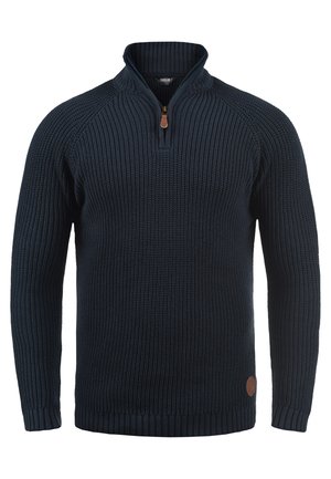 Navy blue knitted sweater with a high collar and half-zip, featuring ribbed cuffs and hem, and a small leather logo patch on the side.