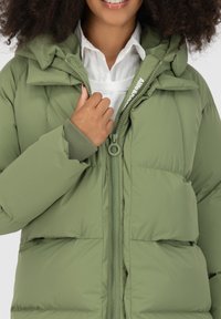 Giacca a vento verde con cappuccio e polsini a coste, dotata di zip centrale e dettagli del logo nel tirazip. Texture morbida e imbottita.