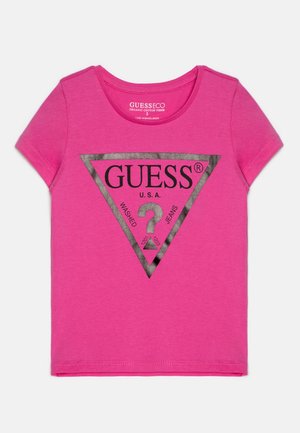 Ροζ βαμβακερό T-shirt με κοντά μανίκια και στρογγυλή λαιμόκοψη. Διαθέτει μαύρο τριγωνικό λογότυπο με την ένδειξη "GUESS" και κείμενο σε μεταλλικό ασημί χρώμα.