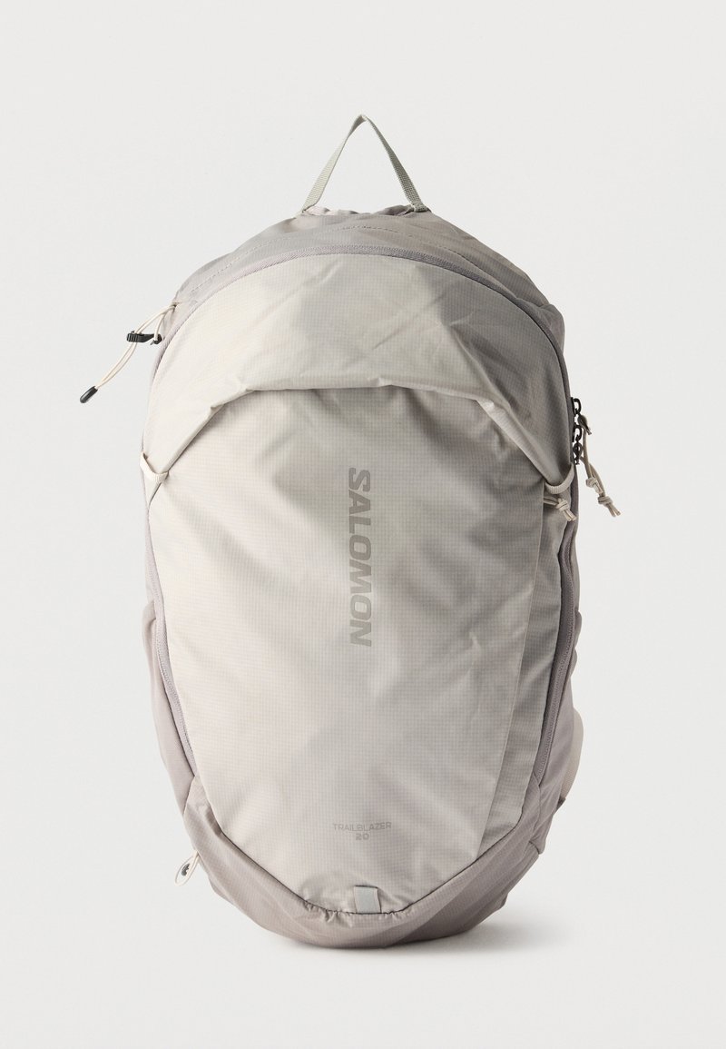 Ανοιχτό γκρι σακίδιο πλάτης Salomon Trailblazer 20 με λαβή μεταφοράς στην κορυφή, εμπρόσθια τσέπη με φερμουάρ και καμπυλωτό σχέδιο σε απλό φόντο.