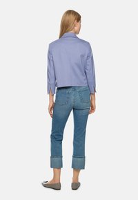 Light purple cropped jacket with three-quarter sleeves, featuring a back vent and a small hardware detail. Paired with light blue cuffed jeans.