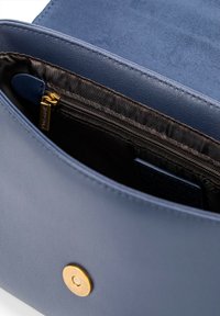 Innenraum einer navy blauen Ledertasche, ausgestattet mit einer Reißverschlusstasche und glattem Futter. Goldfarbene Hardware-Akzente mit einem Druckknopfverschluss.
