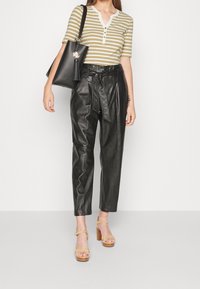 Randig grön och vit kortärmad skjorta, svarta läderbyxor med hög midja, bruna sandaler och svart väska med tofsdetalj.