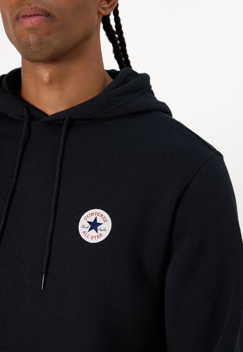 Sudadera negra de algodón, con un logo bordado redondo que muestra una estrella azul y el texto rojo "CONVERSE ALL STAR" en el pecho.