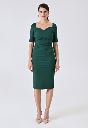 Grünes, tailliertes Kleid mit kurzen Ärmeln und herzförmigem Ausschnitt. Glatte Textur, knielang, kombiniert mit beigen, spitzen Absatzschuhen und Knöchelriemen.