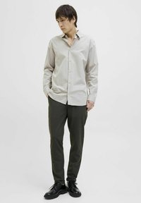 Cămașă crem cu dungi fine, cu o croială lejeră, guler cu nasturi și mâneci lungi, asortată cu pantaloni tapered verzi închisi și pantofi negri.
