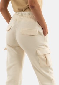 Pantalones cargo beige con una textura suave, que cuentan con dos bolsillos laterales, dos bolsillos traseros y una cintura elástica con detalles del logo.