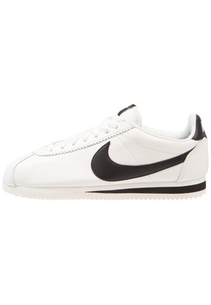 Baskets basses blanches avec virgule Nike noire, lacets blancs et semelle rainurée, vues de profil sur fond blanc.