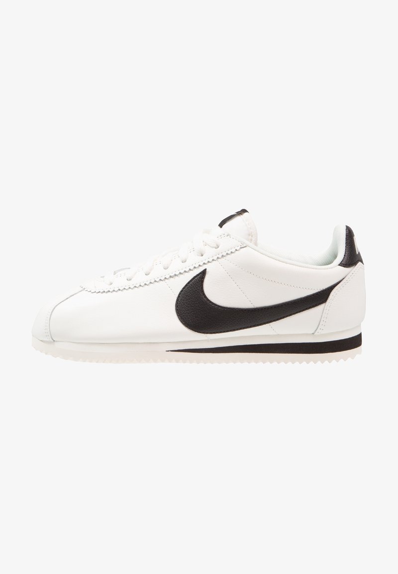 Baskets basses blanches avec virgule Nike noire, lacets blancs et semelle rainurée, vues de profil sur fond blanc.