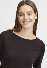 Pull en tricot noir avec un col large et des manches raglan, présentant une texture lisse et une coupe ajustée.