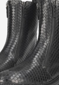 Black leather boots with a textured, scaled pattern, featuring two side zippers for easy wear and a smooth, curved shape.