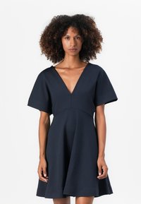 Vestido azul marino con un escote en V profundo, mangas cortas y anchas, y un corpiño ajustado que se ensancha en una falda de vuelo. Textura suave, diseño minimalista.
