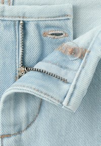 Svetlomodrá rifľovina s otvoreným kovovým zipsom, priehľadným plastovým gombíkom a prišitým gombíkovým dierkovým detailom zblízka.