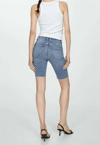 Vaaleansiniset farkkushortsit, joissa on istuva malli, hieman polven ylle. Takana on taskut ja korkeavyötäröinen malli, yhdistettynä mustiin korkokenkiin.