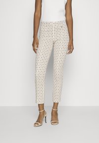 Hvide ankel-lange bukser med et geometrisk mønster i blå og gul. Stoffet har en glat tekstur og er parret med beige hæle-sandaler.