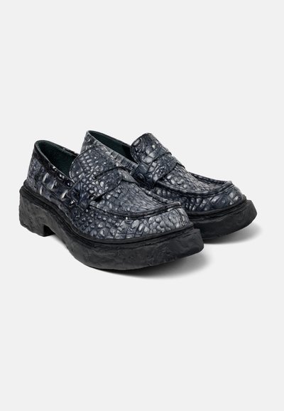 Black textured loafers with a crocodile pattern, featuring a broad strap and a thick, rugged sole. Smooth interior lining.