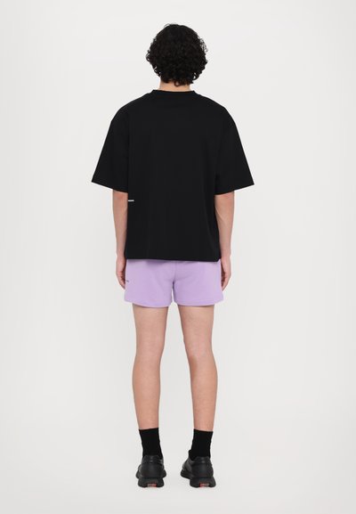 Camiseta de algodón negra con mangas cortas, combinada con pantalones cortos de color púrpura claro. Unos zapatos negros completan el conjunto, con un diseño sencillo y sin patrones visibles.
