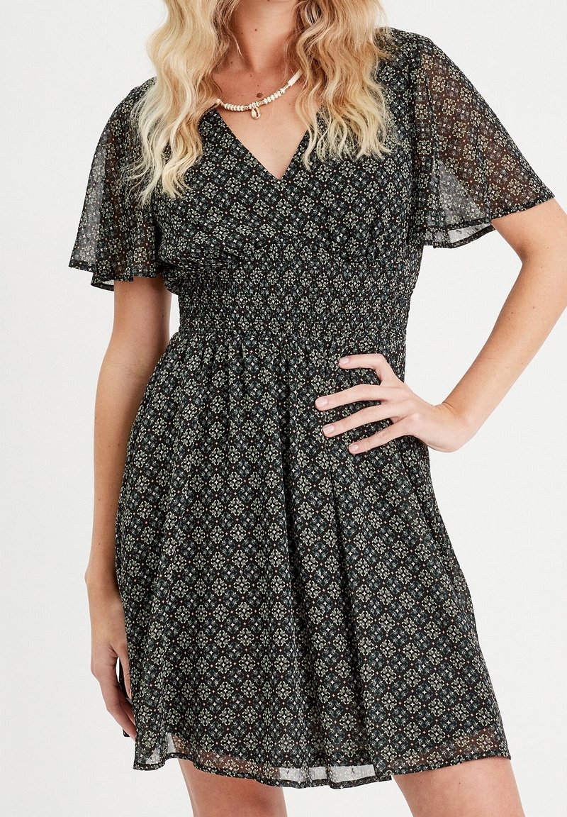 Robe noire à fleurs avec une taille smockée, des manches flottantes transparentes et un décolleté en V. Elle présente un motif dans des tons rouges et verts.