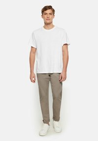 Weißes Baumwoll-T-Shirt kombiniert mit hellbeigen Chinos. Das Modell trägt weiße Sneakers. Einfaches Design mit kurzen Ärmeln und umgeschlagenen Säumen an den Hosen.