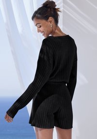 Zwart geribbeld breisel loungewear-set bestaande uit een loose-fit, lange mouwen top en shorts met een elastische tailleband, met een gestructureerd oppervlak.