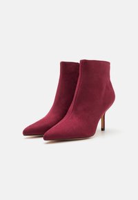 Botines de ante burdeos con punta afilada y tacón de aguja delgado; textura suave con una silueta elegante y sin cierres visibles.