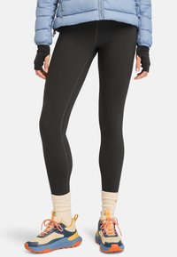 Svarta leggings med kontrasterande sömmar, bärs med färgglada sneakers och krämfärgade strumpor. Outfiten är lager-på-lager med en ljusblå puffjacka.
