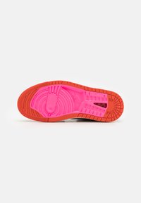 Shoe sole featuring a vibrant pink rubber bottom with circular and linear tread patterns, accented by an orange edge for traction.