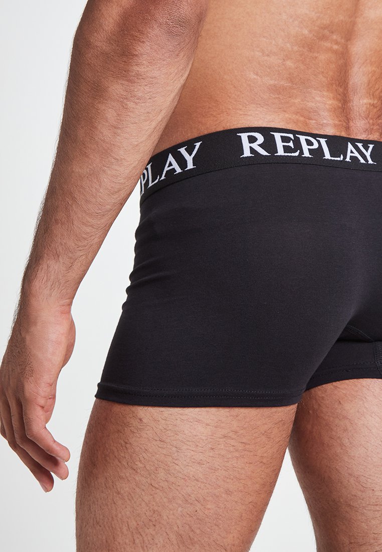 Schwarze Baumwoll-Boxershorts mit breitem weißem „REPLAY“-Logo-Bund. Glatte Textur und enganliegendes Design, hervorgehoben durch eine Seitenansicht.