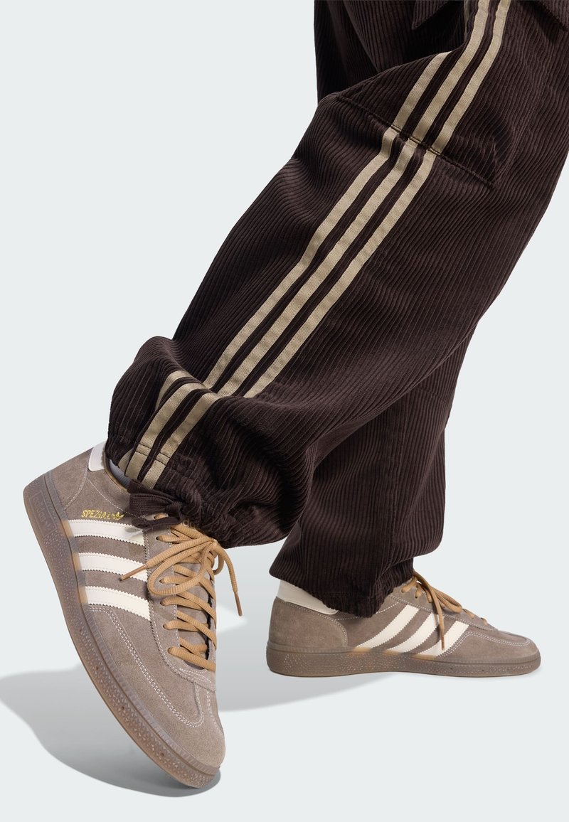 Fødder iført beige Adidas Spezial sneakers og brune fløjlsbukser med beige sidelister på en lys baggrund.